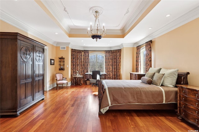 bedroom featuring hardwood / wood-style flooring, a notable chandelier, a raised ceiling, and crown molding