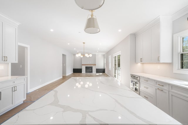 kitchen featuring hanging light fixtures, white cabinetry, stainless steel oven, and light stone counters