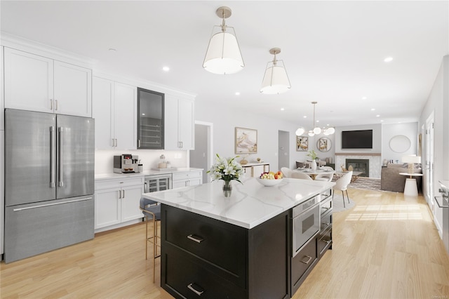 kitchen with appliances with stainless steel finishes, wine cooler, white cabinets, a kitchen island, and light wood-type flooring