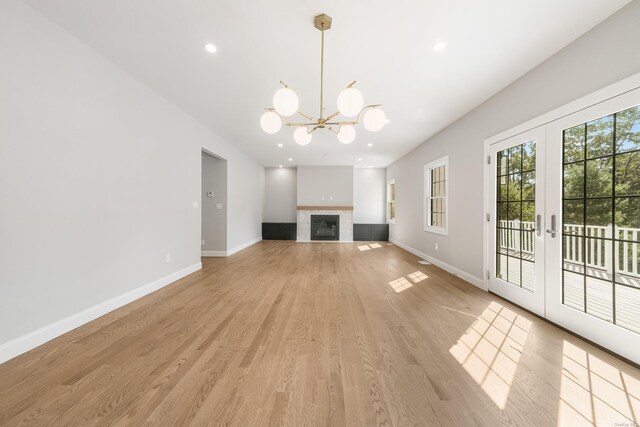 unfurnished living room featuring a tiled fireplace, a notable chandelier, french doors, and light wood-type flooring