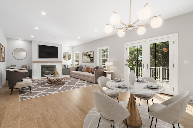 dining space featuring french doors, a fireplace, an inviting chandelier, and light hardwood / wood-style flooring