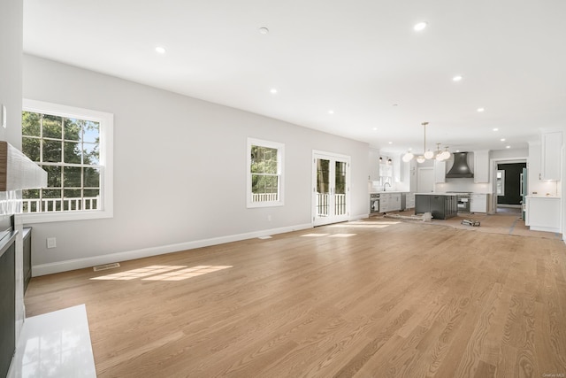 unfurnished living room featuring sink, a notable chandelier, and light hardwood / wood-style flooring