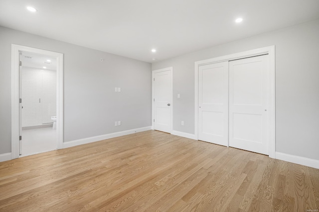 unfurnished bedroom with ensuite bath, a closet, and light wood-type flooring