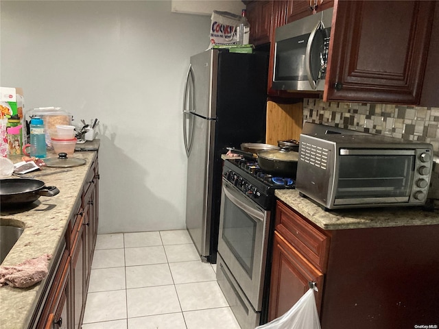 kitchen with backsplash, light stone counters, light tile patterned flooring, and stainless steel appliances