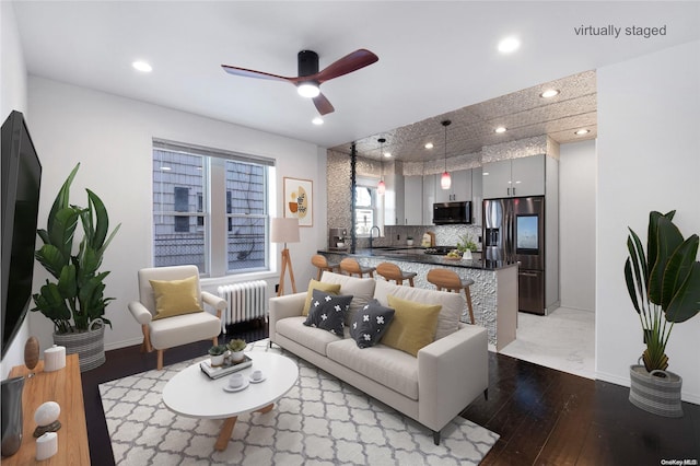 living room featuring radiator heating unit, light wood-type flooring, ceiling fan, and sink