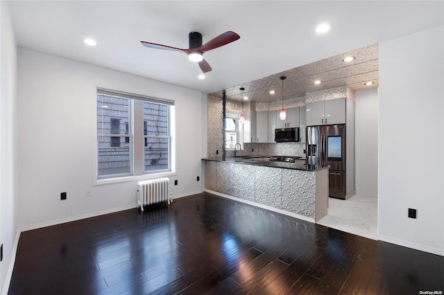 kitchen featuring sink, radiator heating unit, kitchen peninsula, decorative light fixtures, and appliances with stainless steel finishes