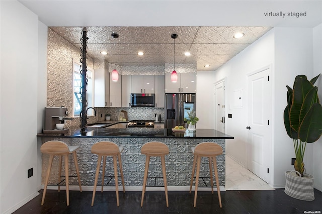 kitchen featuring sink, stainless steel appliances, kitchen peninsula, decorative light fixtures, and a breakfast bar area