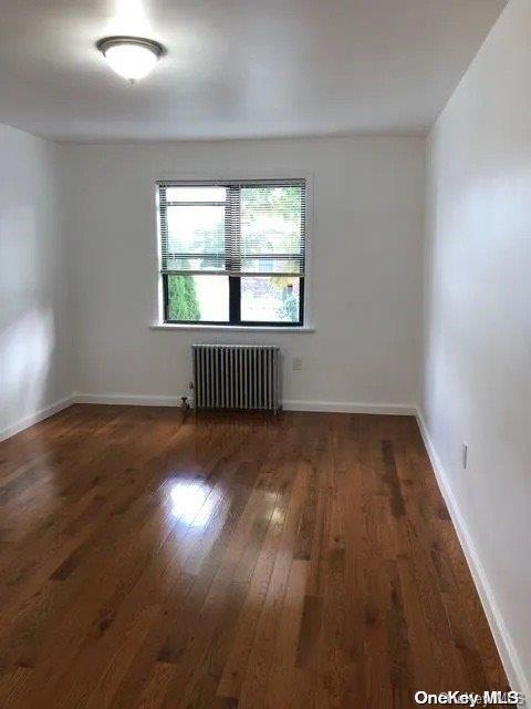 spare room with dark hardwood / wood-style flooring and radiator