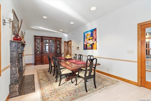 dining area with a premium fireplace, ornamental molding, and light hardwood / wood-style flooring