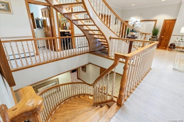 staircase with a chandelier, hardwood / wood-style flooring, baseboard heating, and crown molding