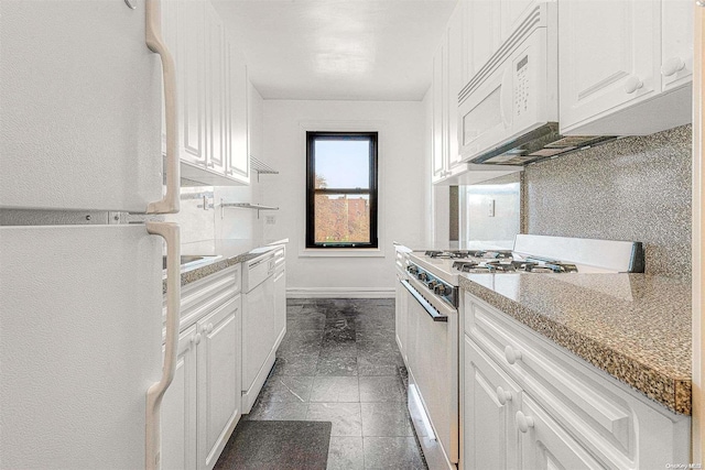 kitchen with light stone counters, dark tile patterned floors, white cabinets, and white appliances