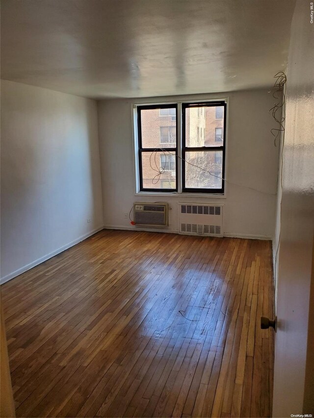 empty room featuring an AC wall unit, radiator, and hardwood / wood-style flooring