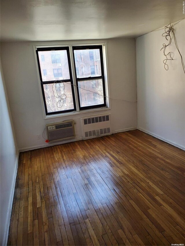 empty room featuring a wall unit AC, radiator heating unit, and dark hardwood / wood-style floors