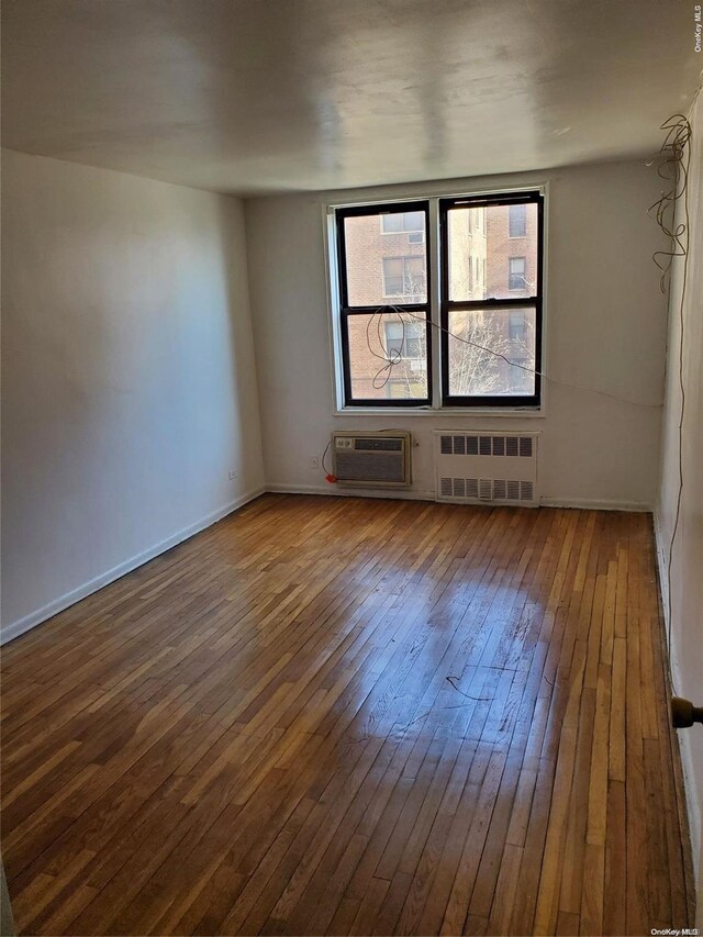 empty room with a wall mounted air conditioner, hardwood / wood-style floors, and radiator