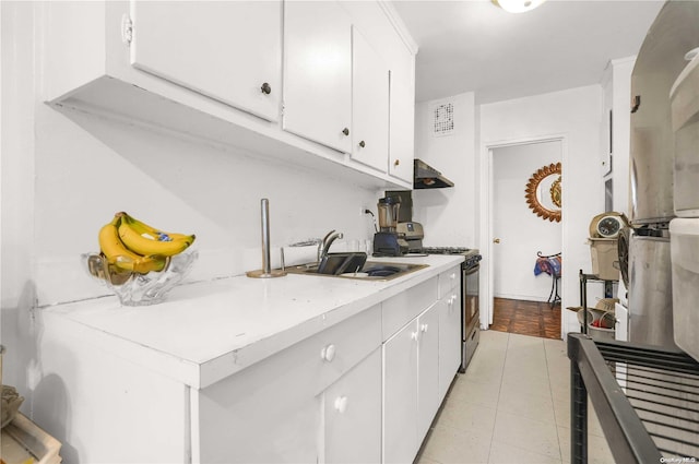 kitchen with wall chimney range hood, sink, stainless steel stove, white cabinetry, and light tile patterned flooring