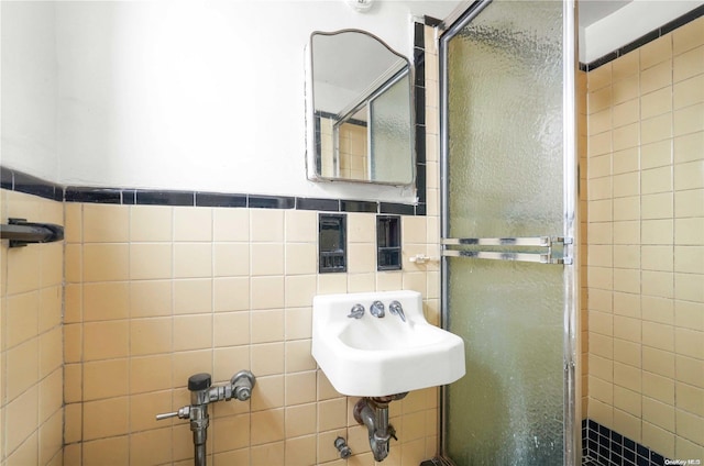 bathroom with a shower with door, tile walls, and sink