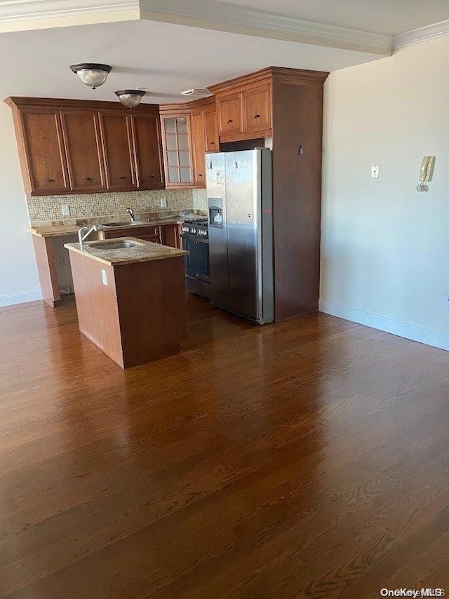 kitchen with appliances with stainless steel finishes, dark hardwood / wood-style flooring, tasteful backsplash, a kitchen island with sink, and crown molding