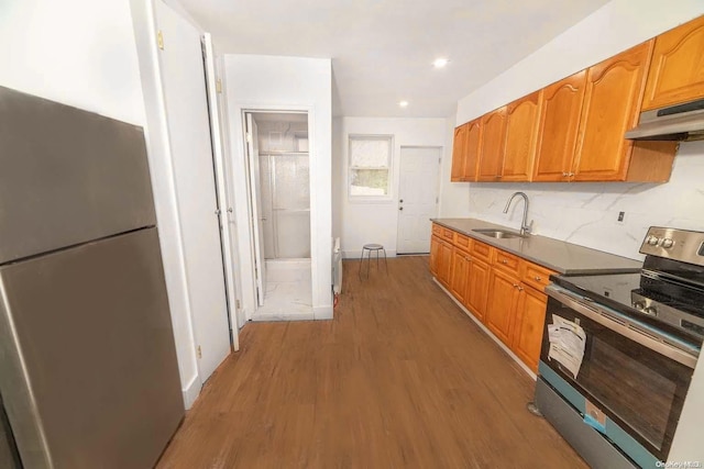 kitchen featuring hardwood / wood-style floors, black electric range oven, stainless steel refrigerator, and sink