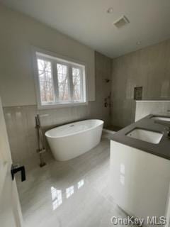 bathroom featuring tile patterned flooring, a bath, tile walls, and sink