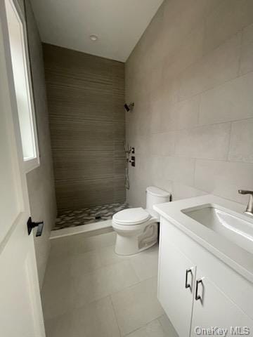 bathroom with vanity, tile patterned floors, toilet, tile walls, and a tile shower