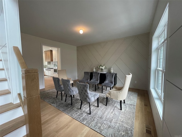 dining area with an accent wall, stairway, wood finished floors, and visible vents