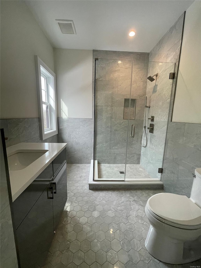 full bathroom with tile walls, visible vents, toilet, a stall shower, and vanity