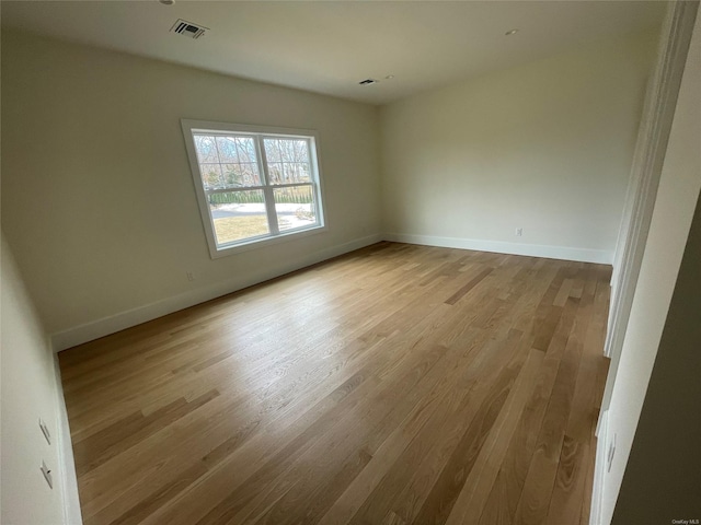 empty room with light wood finished floors, visible vents, and baseboards