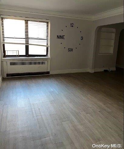 spare room with wood-type flooring, radiator heating unit, and crown molding