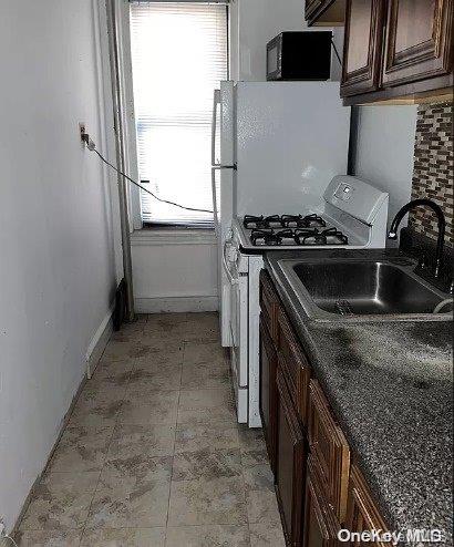 kitchen featuring dark stone countertops, dark brown cabinetry, white gas stove, and sink