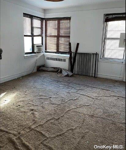 carpeted empty room featuring plenty of natural light, cooling unit, and radiator heating unit