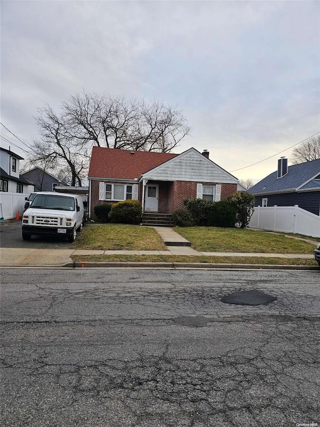 view of front of property featuring a lawn, brick siding, and fence