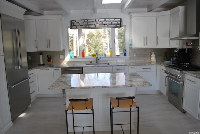 kitchen with sink, wall chimney range hood, high quality appliances, a breakfast bar, and white cabinets