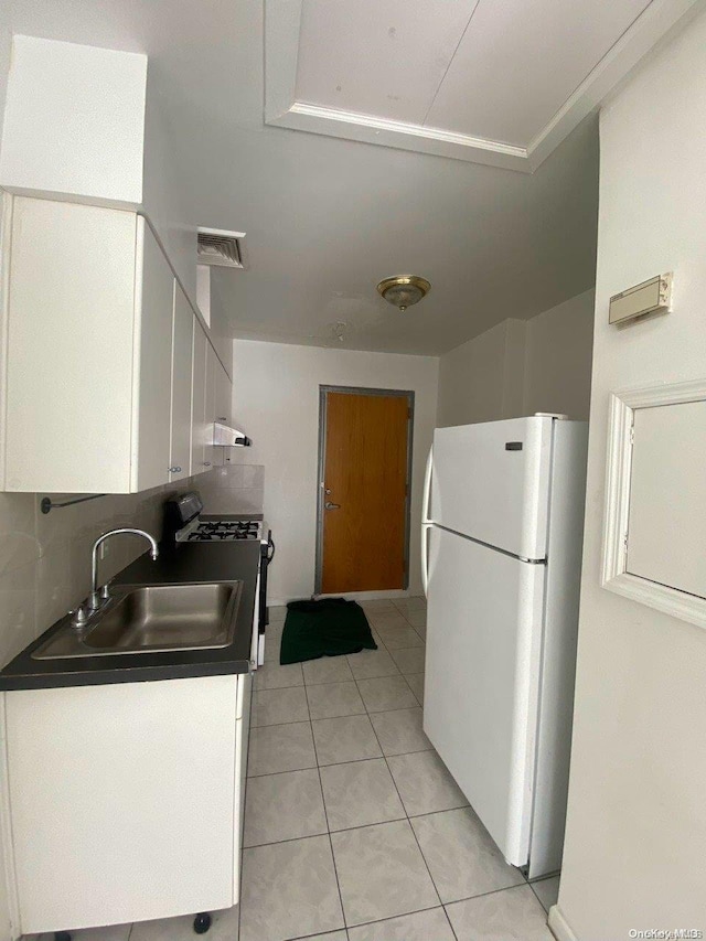 kitchen featuring sink, gas range, light tile patterned floors, white fridge, and white cabinetry