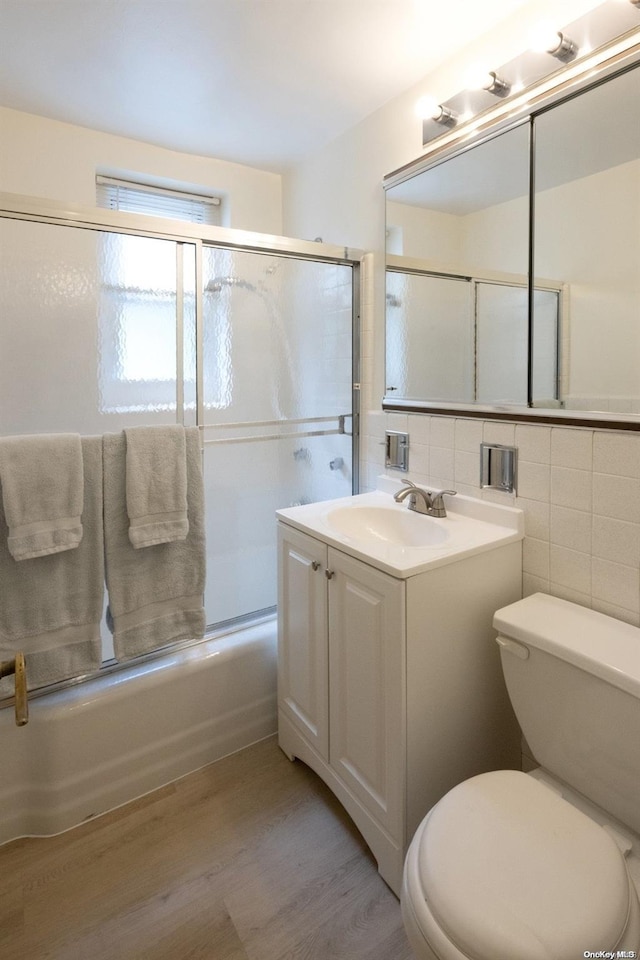 full bathroom featuring vanity, bath / shower combo with glass door, toilet, tile walls, and wood-type flooring