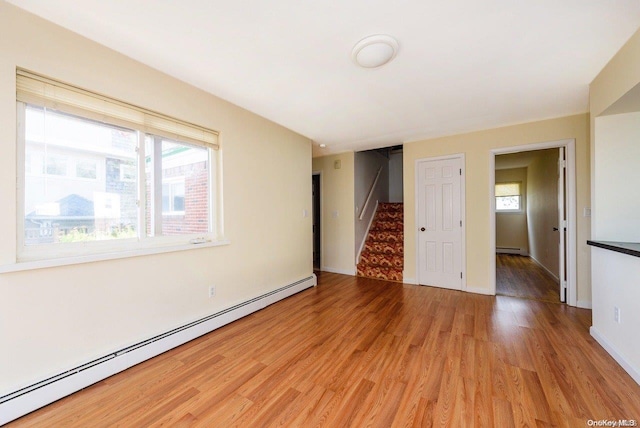 empty room with light wood-type flooring, a baseboard radiator, and plenty of natural light