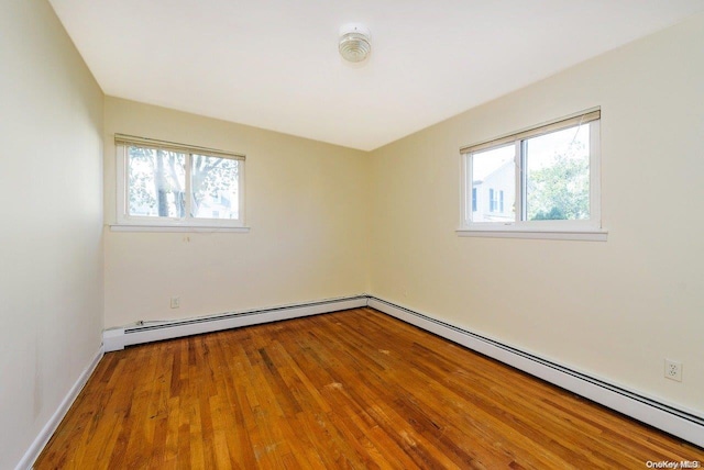 empty room featuring hardwood / wood-style floors, plenty of natural light, and a baseboard heating unit