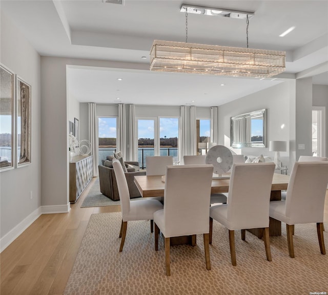 dining room with light hardwood / wood-style flooring, a water view, and a chandelier