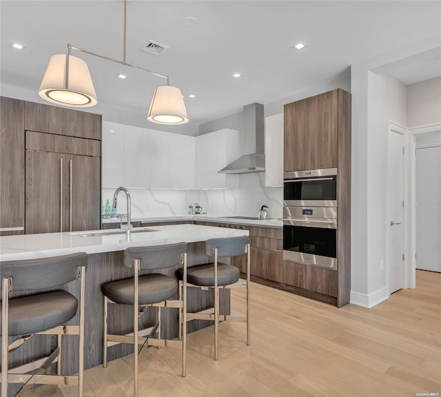 kitchen featuring pendant lighting, a breakfast bar, wall chimney range hood, light hardwood / wood-style floors, and white cabinetry