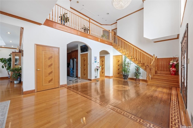 unfurnished living room featuring a towering ceiling, wood-type flooring, and ornamental molding