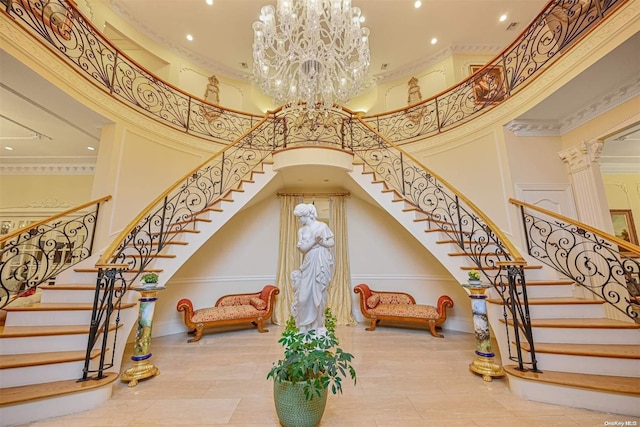 stairway featuring a notable chandelier, a towering ceiling, ornamental molding, and ornate columns