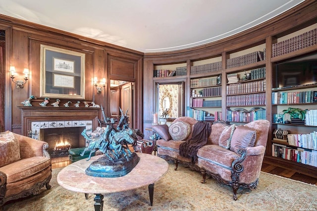 sitting room featuring ornamental molding, built in shelves, a tile fireplace, hardwood / wood-style flooring, and wood walls