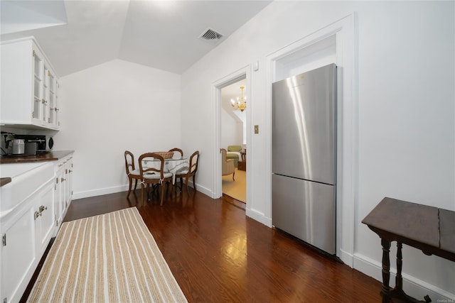 kitchen with stainless steel refrigerator, white cabinetry, dark wood-type flooring, a chandelier, and vaulted ceiling