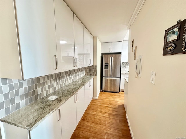 kitchen with decorative backsplash, stainless steel refrigerator with ice dispenser, light wood-type flooring, light stone counters, and white cabinetry