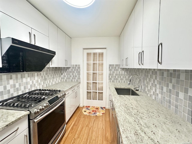 kitchen featuring stainless steel gas range oven, white cabinets, sink, decorative backsplash, and light hardwood / wood-style floors