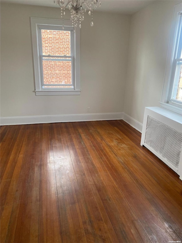 empty room with a chandelier, radiator, baseboards, and dark wood-style flooring