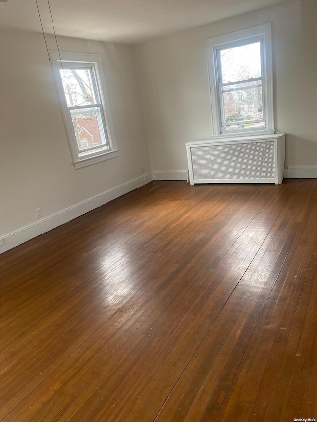 unfurnished room featuring radiator, baseboards, and dark wood-style flooring