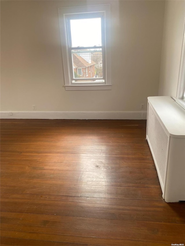 spare room featuring dark wood-style floors, baseboards, and radiator