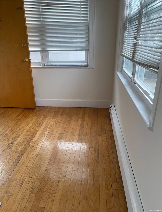 unfurnished room featuring a baseboard heating unit, baseboards, and light wood finished floors