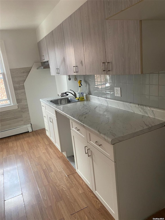 kitchen with light wood-style flooring, light stone countertops, a sink, baseboard heating, and decorative backsplash