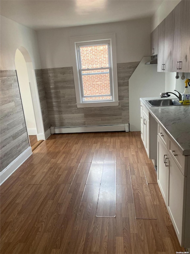 kitchen featuring a baseboard radiator, light countertops, white cabinets, a sink, and light wood-type flooring